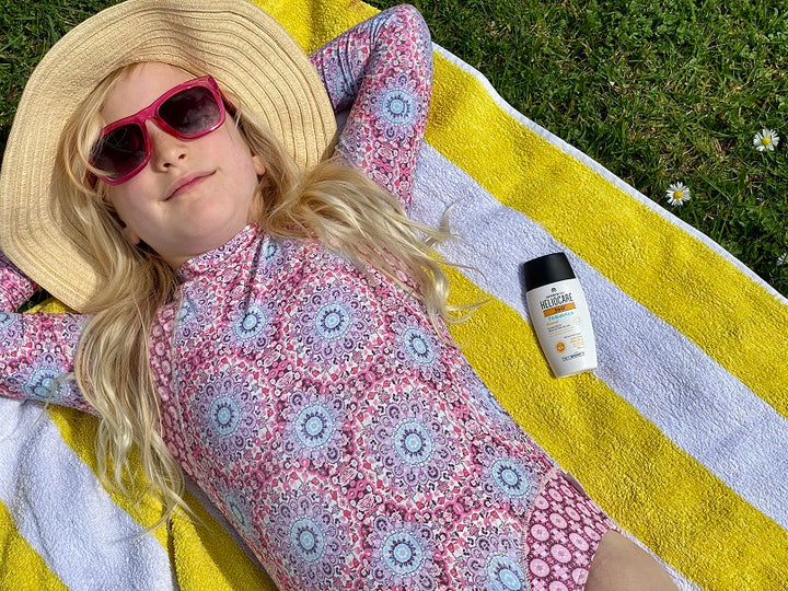 Heliocare girl laying in sun on beachtowel with Heliocare Pediatrics Mineral Sunscreen with Fernblock and Niacinamide brought to New Zealand by Solafern Ltd